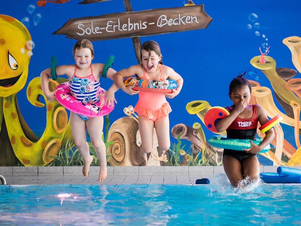 Drei Mädchen mit Schwimmreifen springen ins Wasser